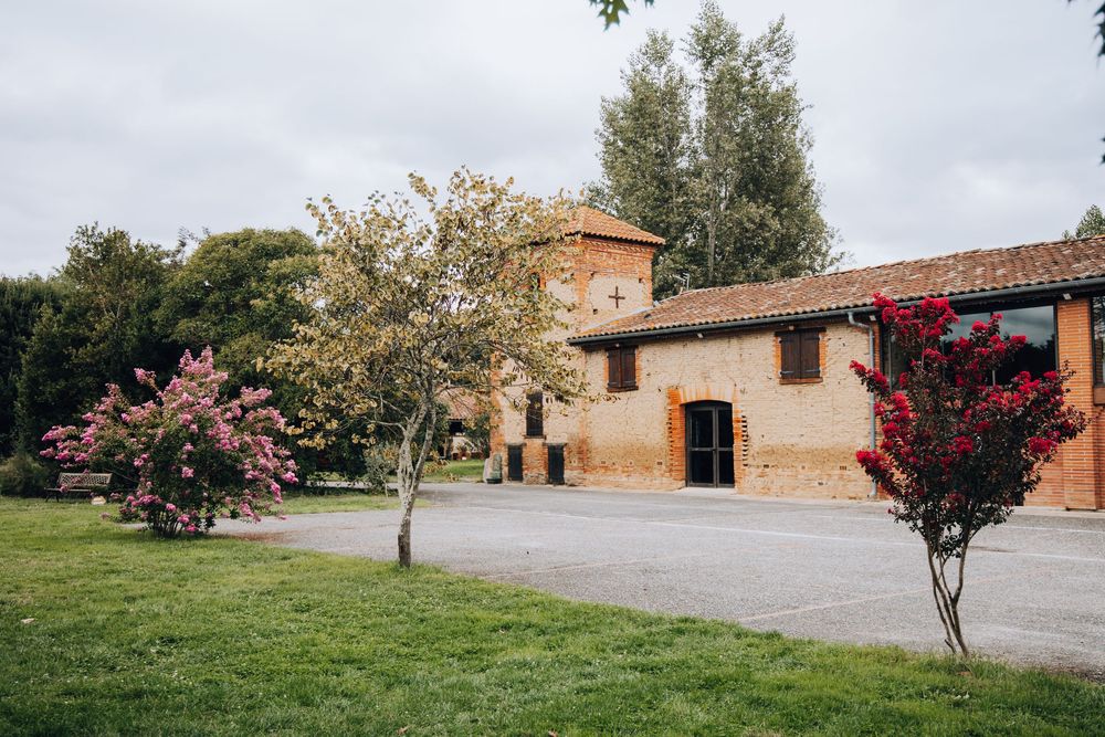 Picturesque rustic brick wedding venue with tower surrounded by colorful flowering trees on green lawn.