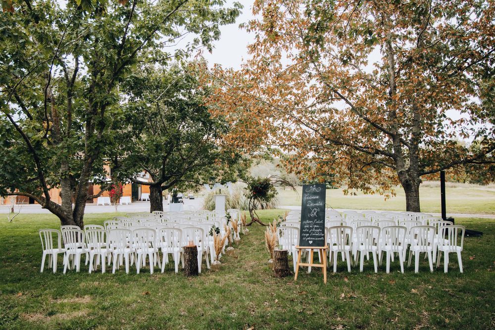 Wide view of outdoor wedding ceremony seating with white chairs arranged on green lawn beneath autumn trees.