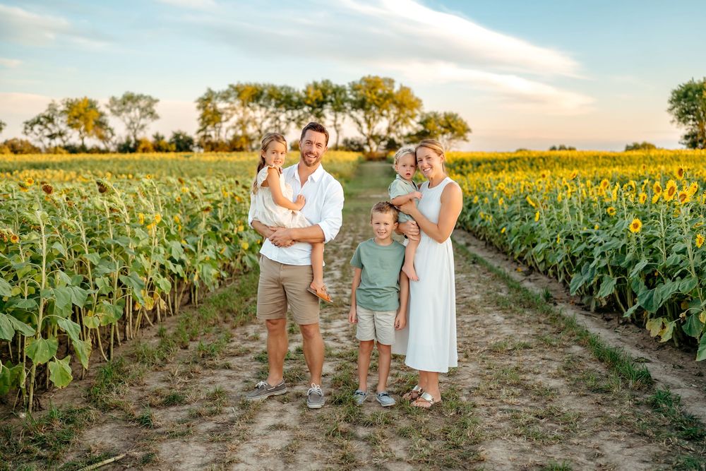 Summer family portrait session among rows of tall sunflowers at sunset.