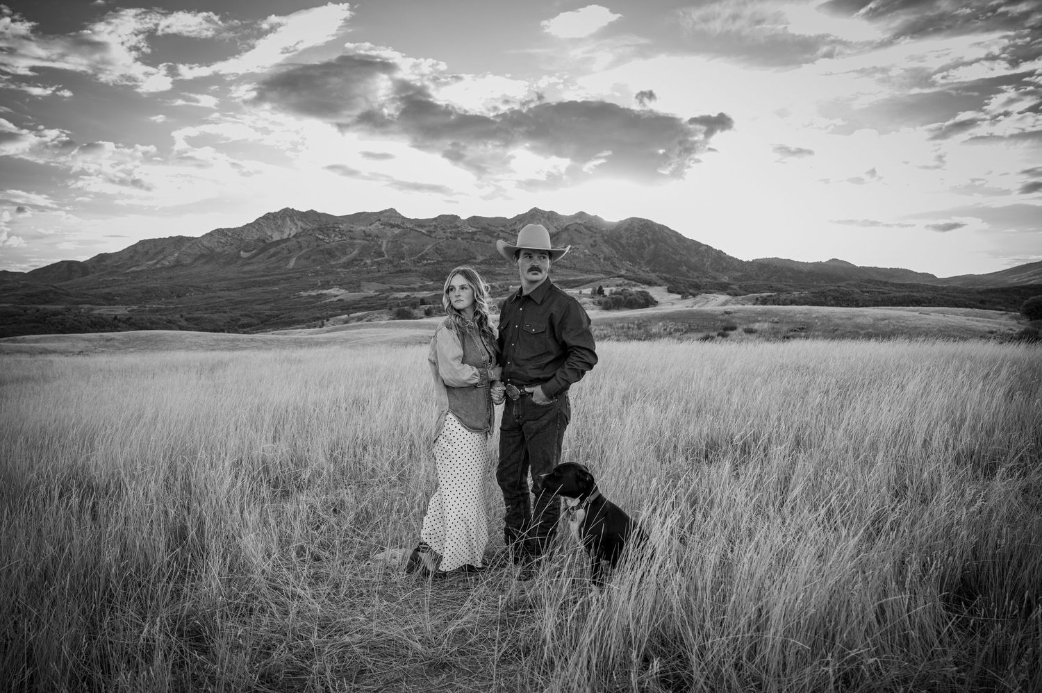 A romantic photoshoot in a scenic mountain field with dramatic clouds and tall grass.