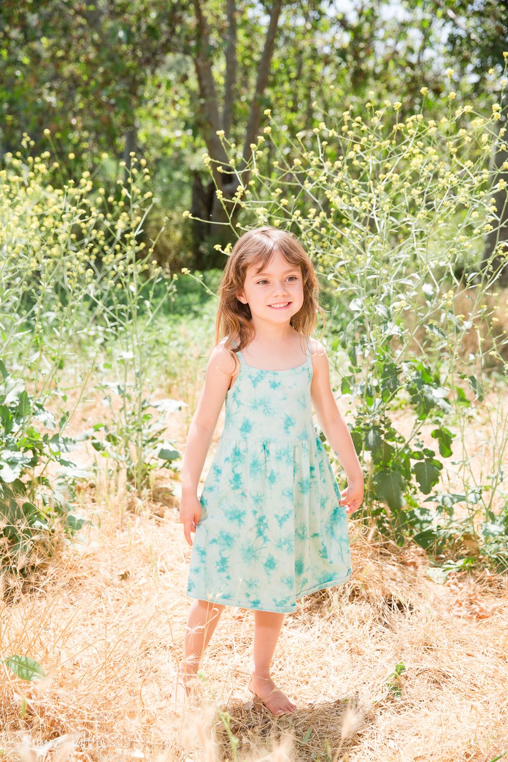 A light turquoise dress stands out against a natural backdrop of wildflowers and sunlit foliage in an outdoor setting.