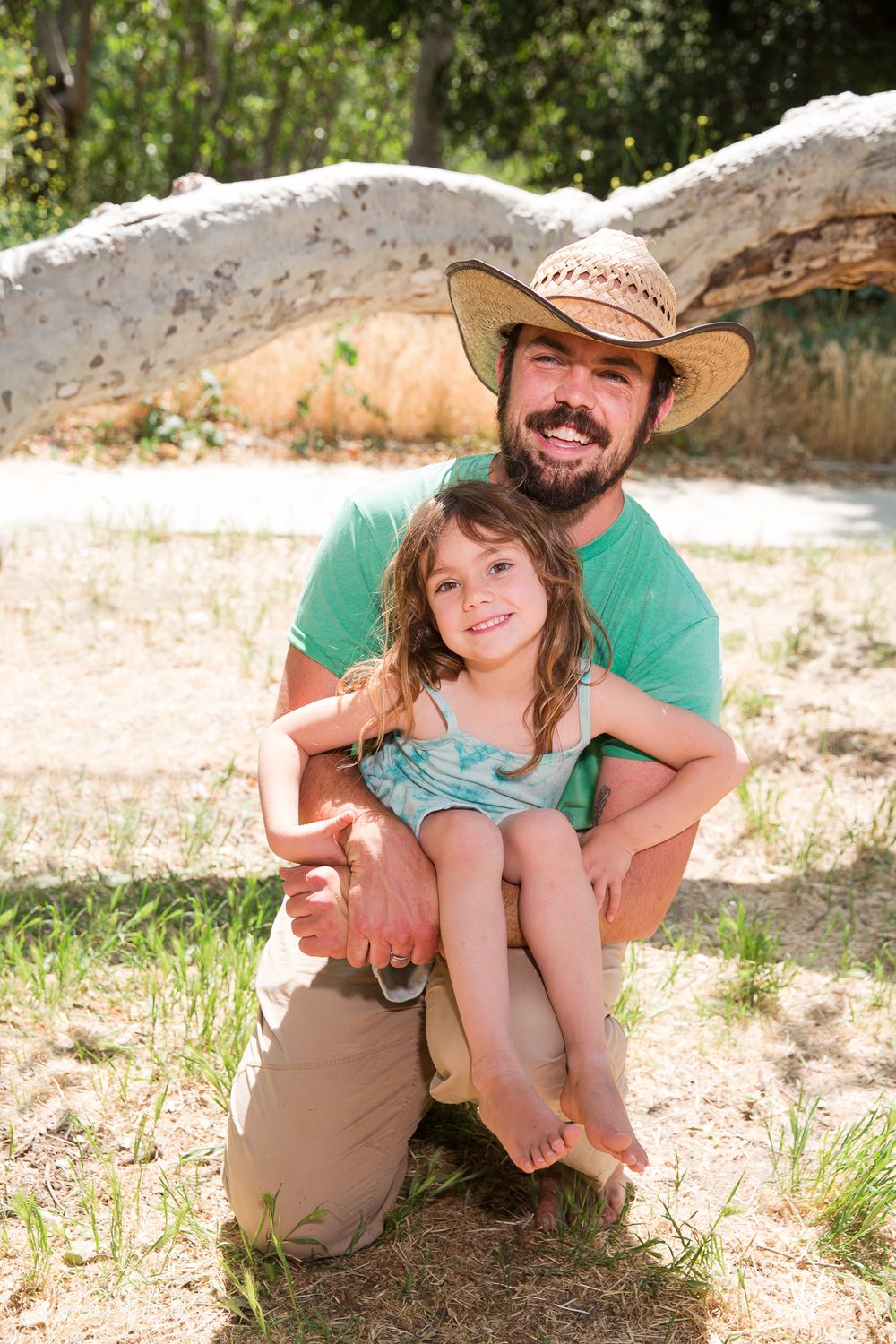 A parent and child share a tender outdoor moment together in sunny weather while sitting on the ground.