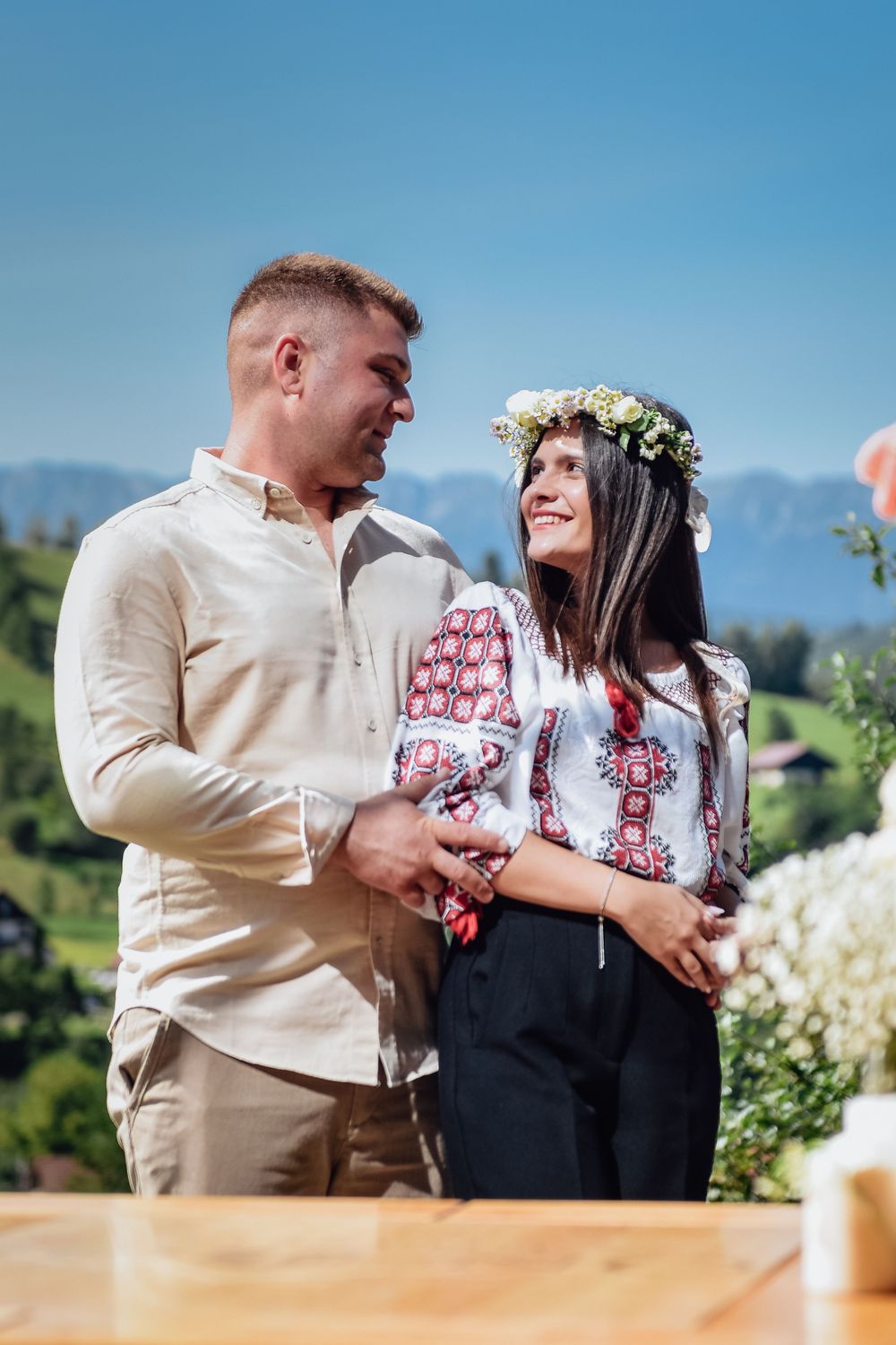 A couple shares a romantic moment in traditional Ukrainian embroidered clothing against a sunny outdoor backdrop.