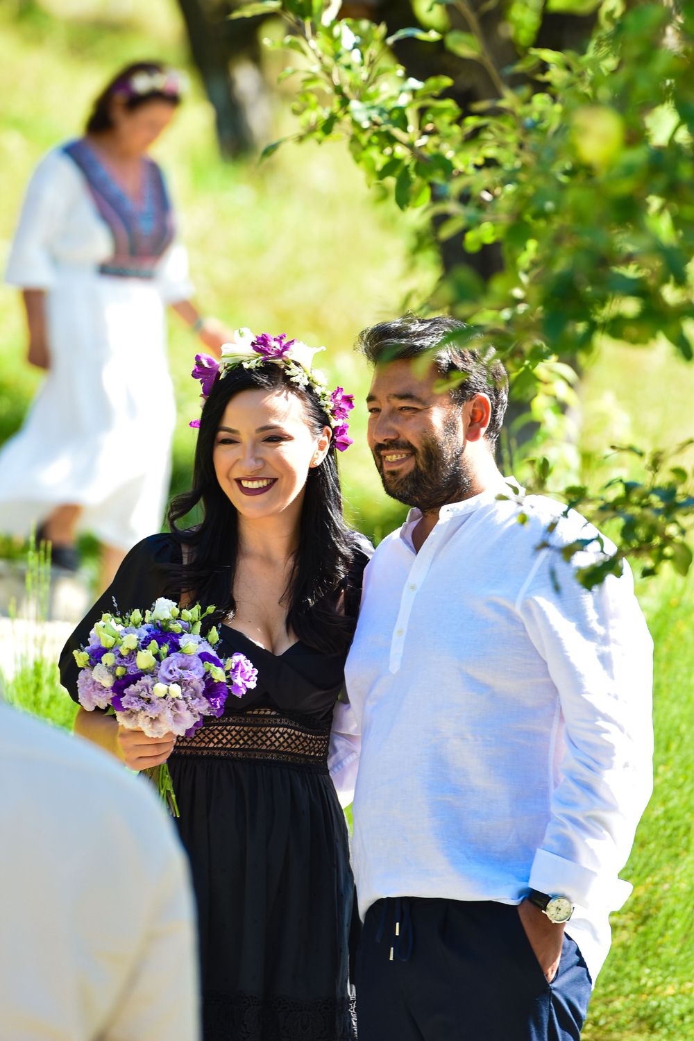 Wedding party members enjoying a casual outdoor gathering under green leafy trees.