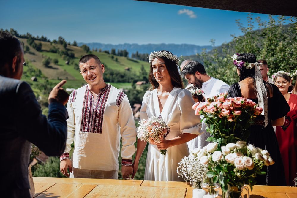 Outdoor wedding celebration in a scenic mountain setting with guests gathered at rustic wooden tables.