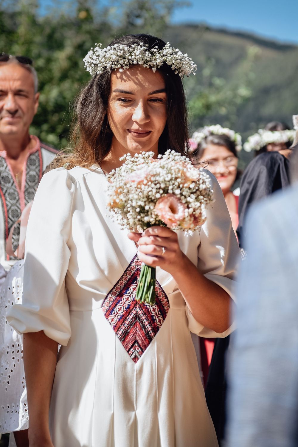 Wedding party members in traditional white embroidered attire hold delicate baby's breath bouquets outdoors.