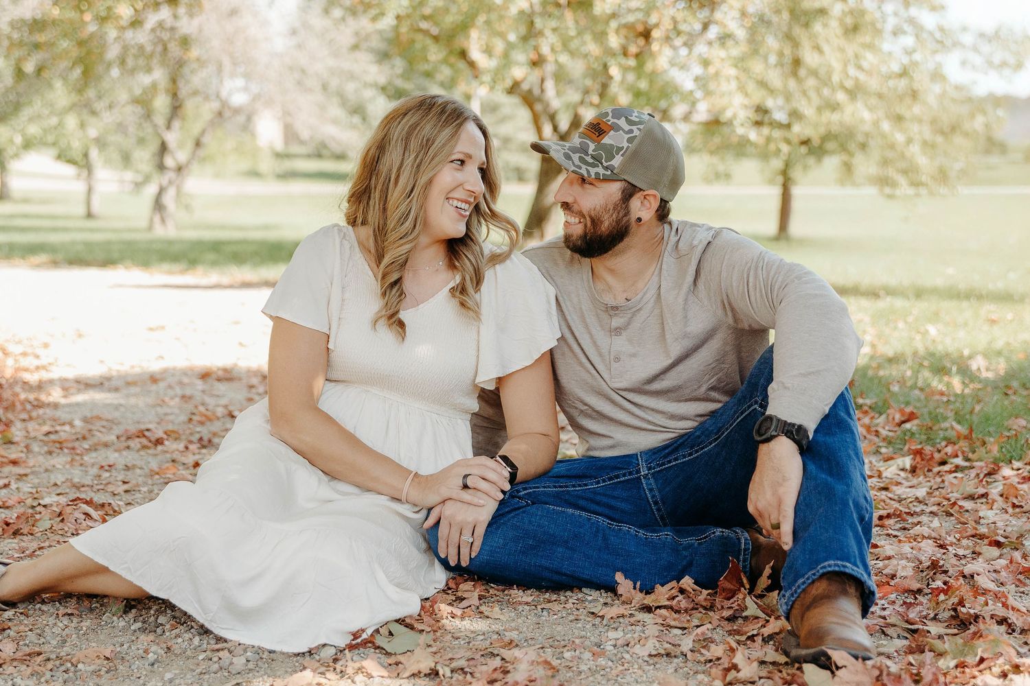 A couple sits together on fallen autumn leaves in a park during a romantic outdoor photoshoot.