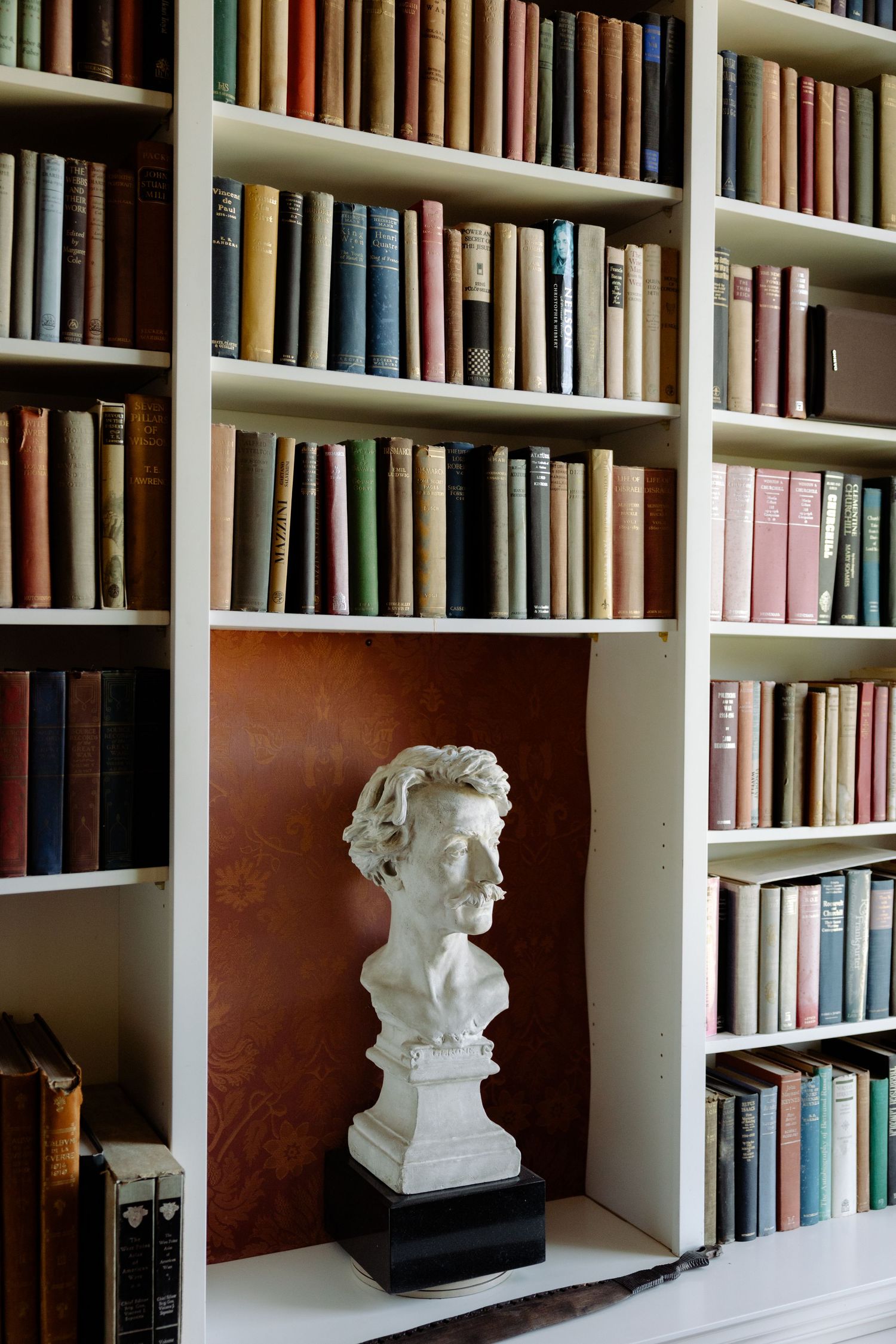 White bookshelves filled with hardcover books and decorative busts create an elegant home library display.