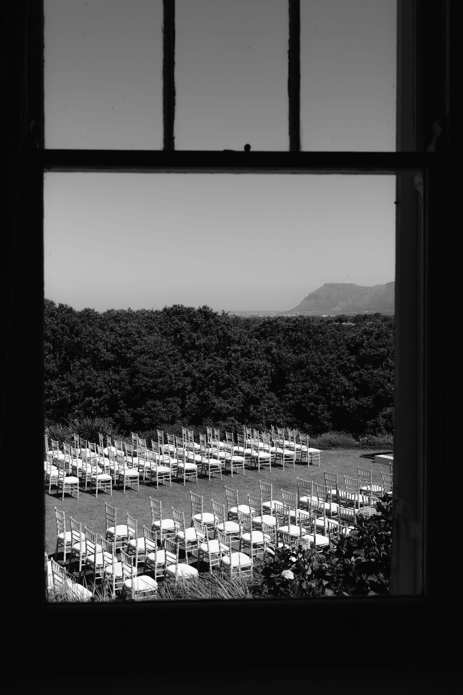 Rows of white chairs set up for an outdoor wedding ceremony with mountain views seen through a window frame.
