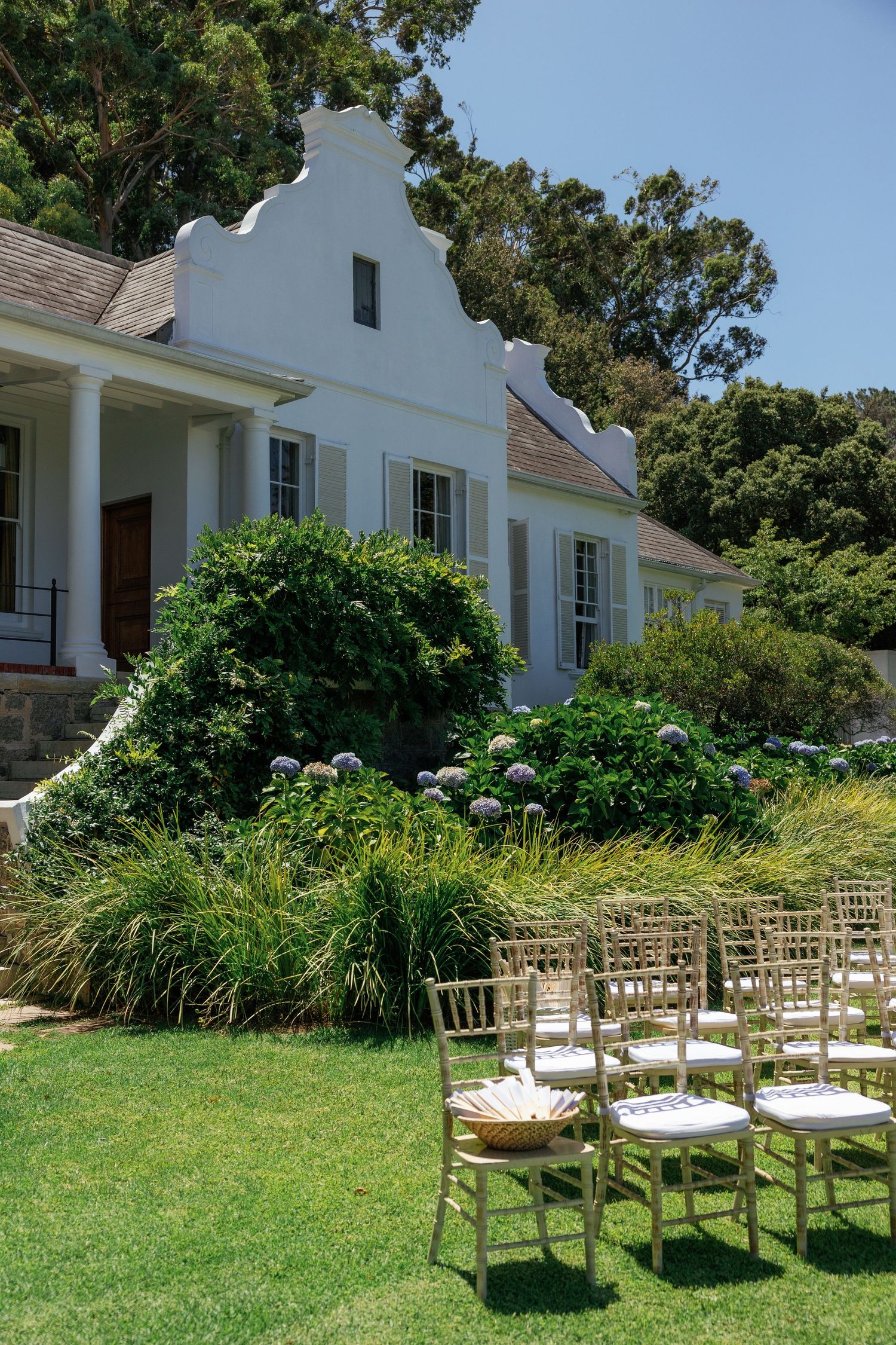 White wooden chairs arranged in rows on a lush green lawn for an outdoor ceremony with a colonial-style building backdrop.