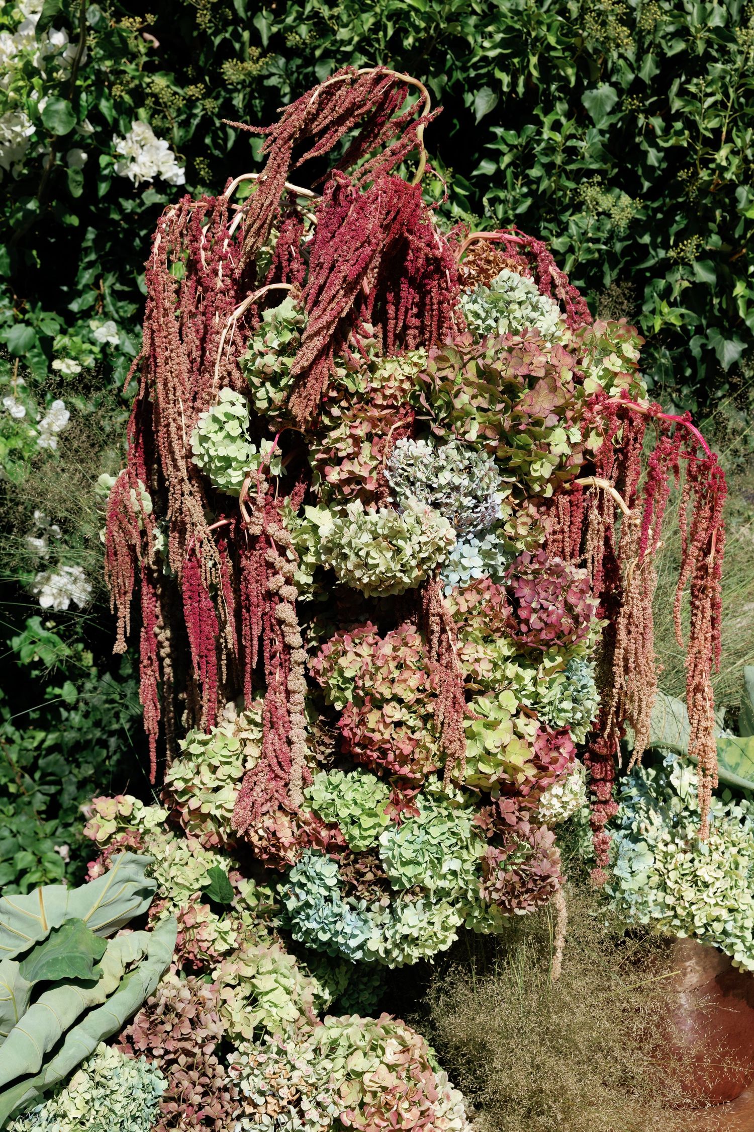 Cascading burgundy amaranthus flowers drape elegantly over a lush garden arrangement with white blooms and greenery.