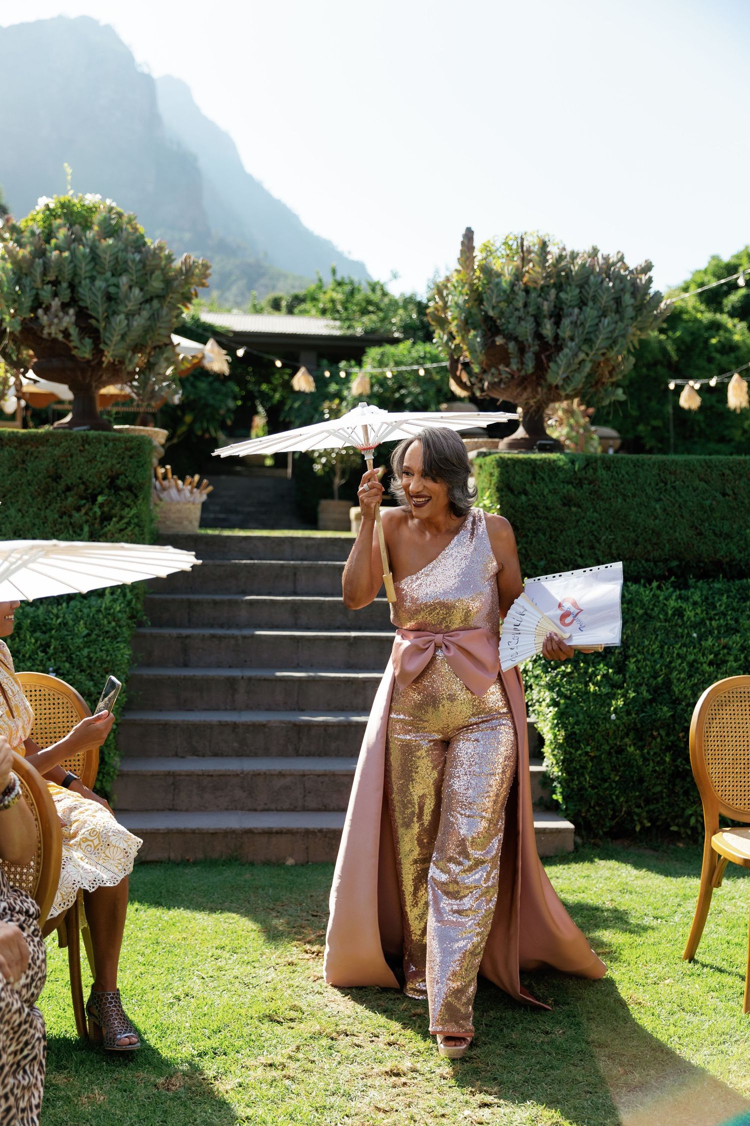Wedding guests enjoy drinks and conversation in an elegant outdoor garden setting with mountain views.