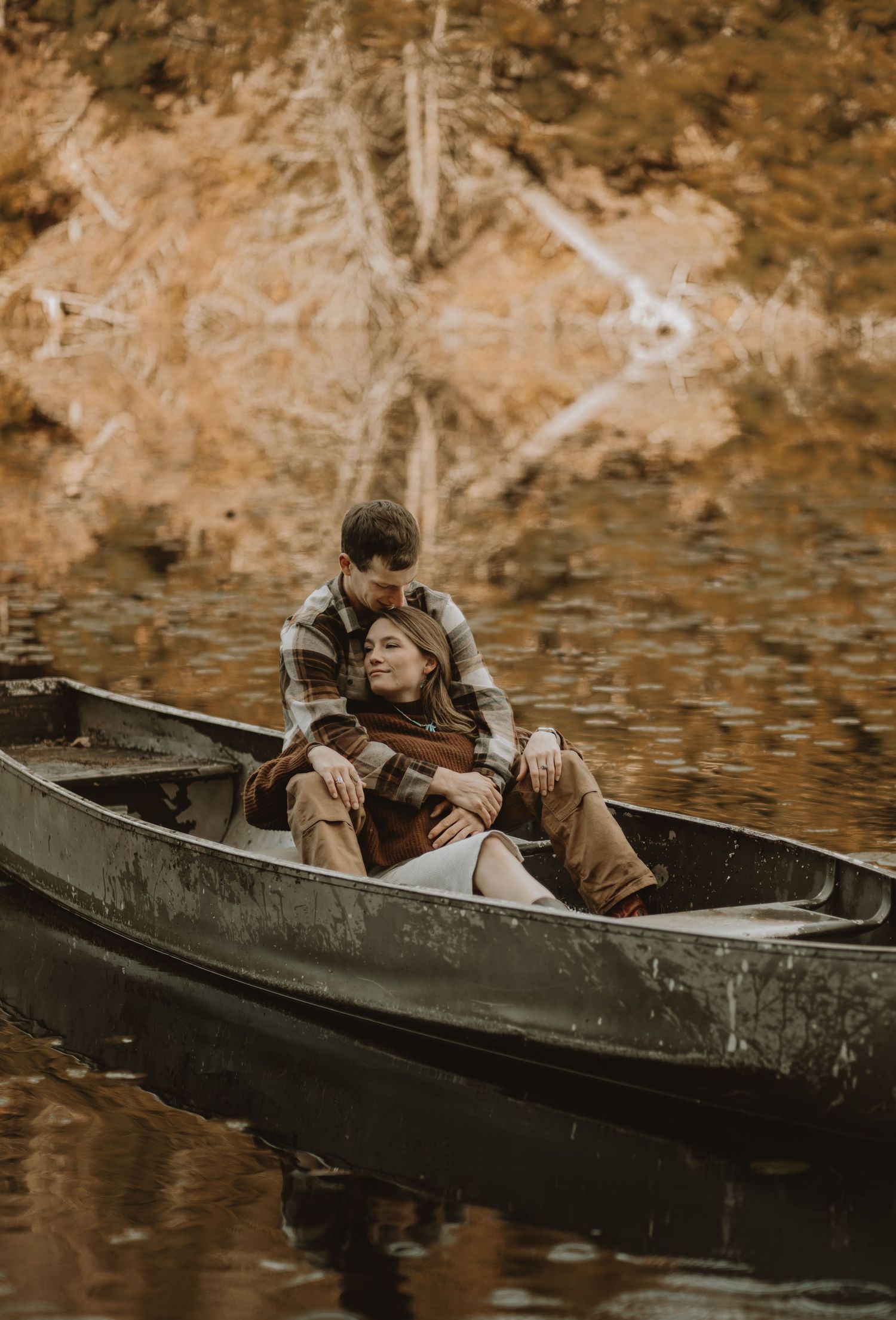 A romantic couple sits together in a canoe on calm autumn waters.