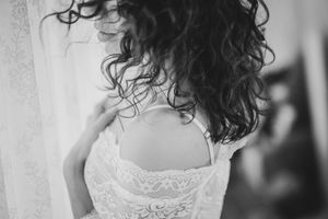A black and white portrait of someone in a lace wedding dress with curly hair and delicate details.