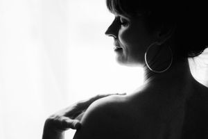 High contrast black and white silhouette profile portrait showing bare shoulder and hoop earring against light background.