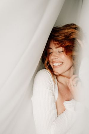 Ethereal portrait series showing joyful expression and flowing hair against soft white fabric background.