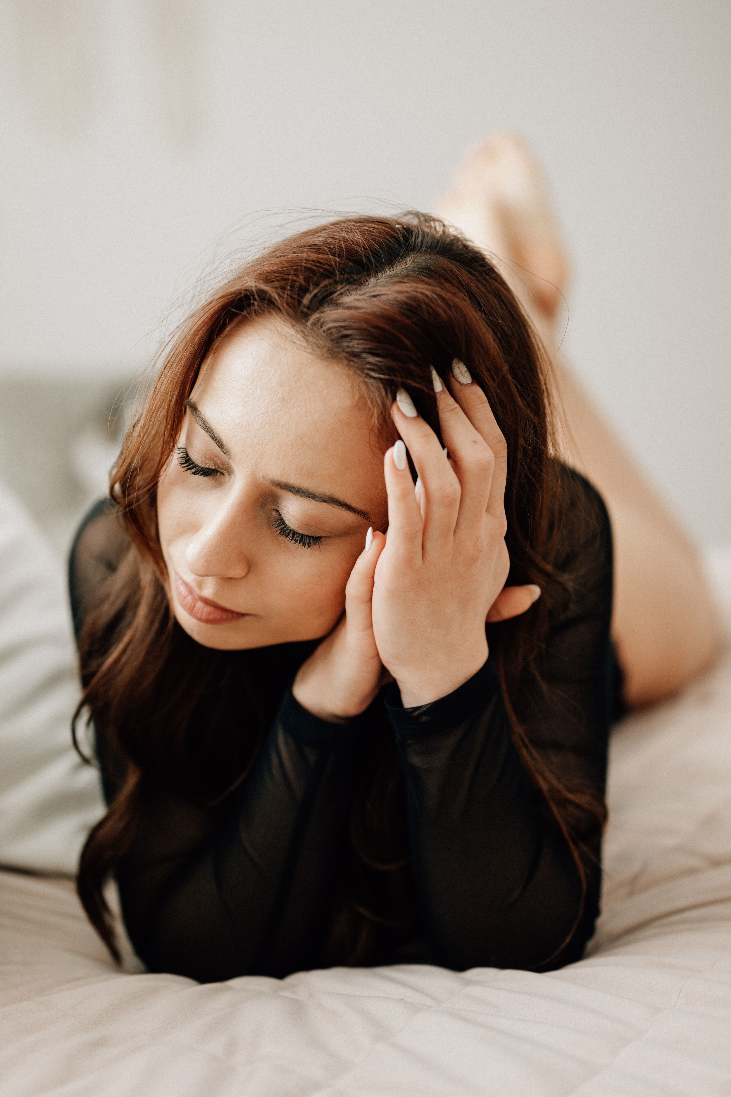 Artistic boudoir photo series showing person in black sweater laying on white bedding with moody lighting.