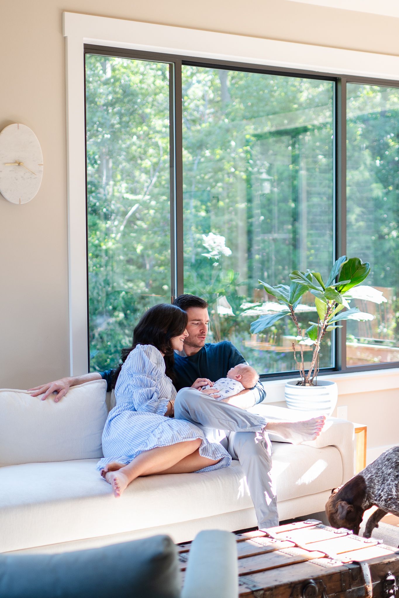 Family sits in their family room as they hold their newborn during their at-home shoot.