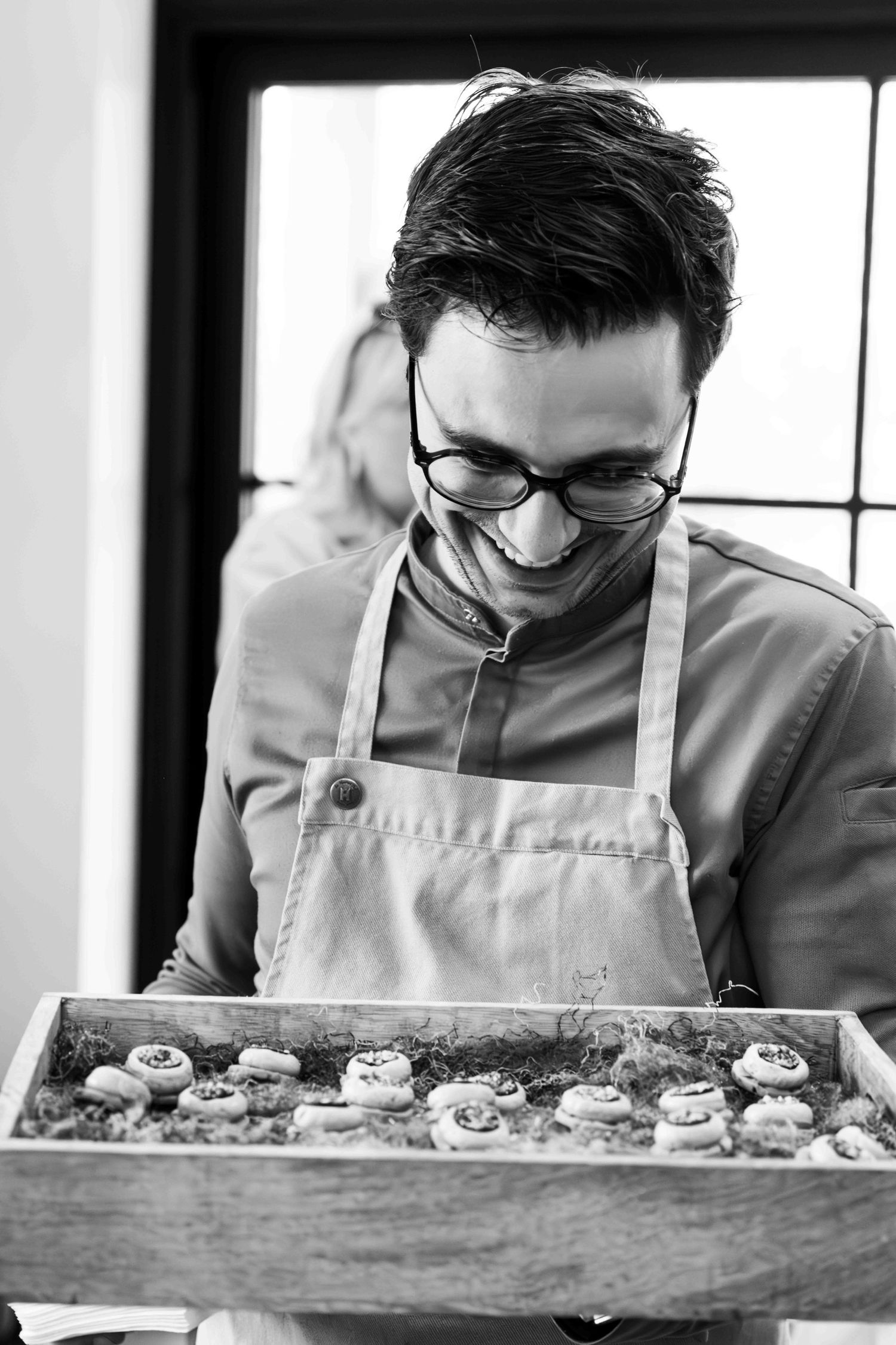 Cook in apron presenting freshly prepared appetizers in wooden tray.