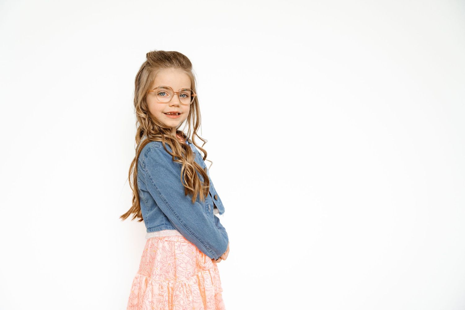 A child in a denim jacket and pink dress poses against a white background.