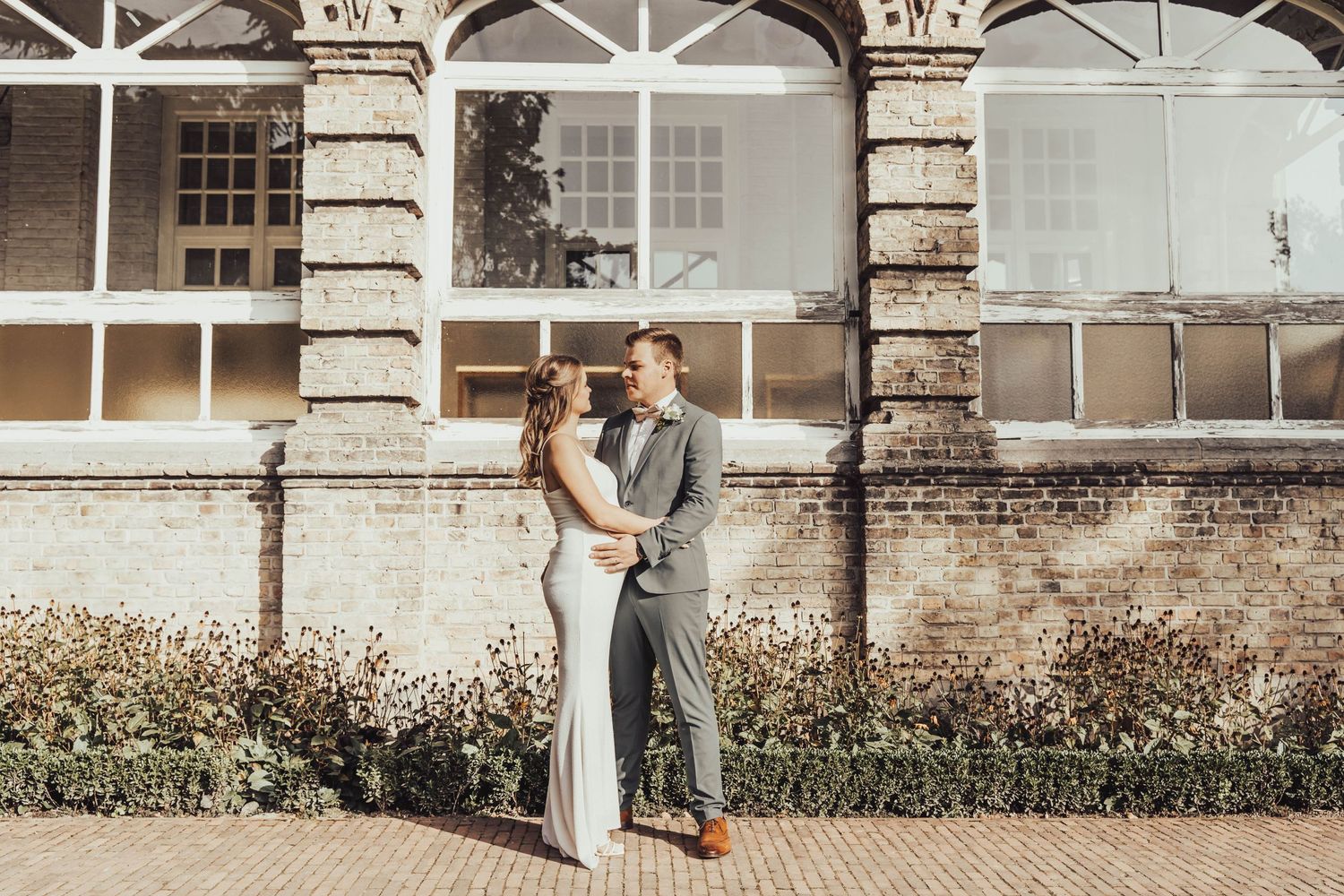 A romantic wedding portrait against a vintage brick building with ornate architectural details.