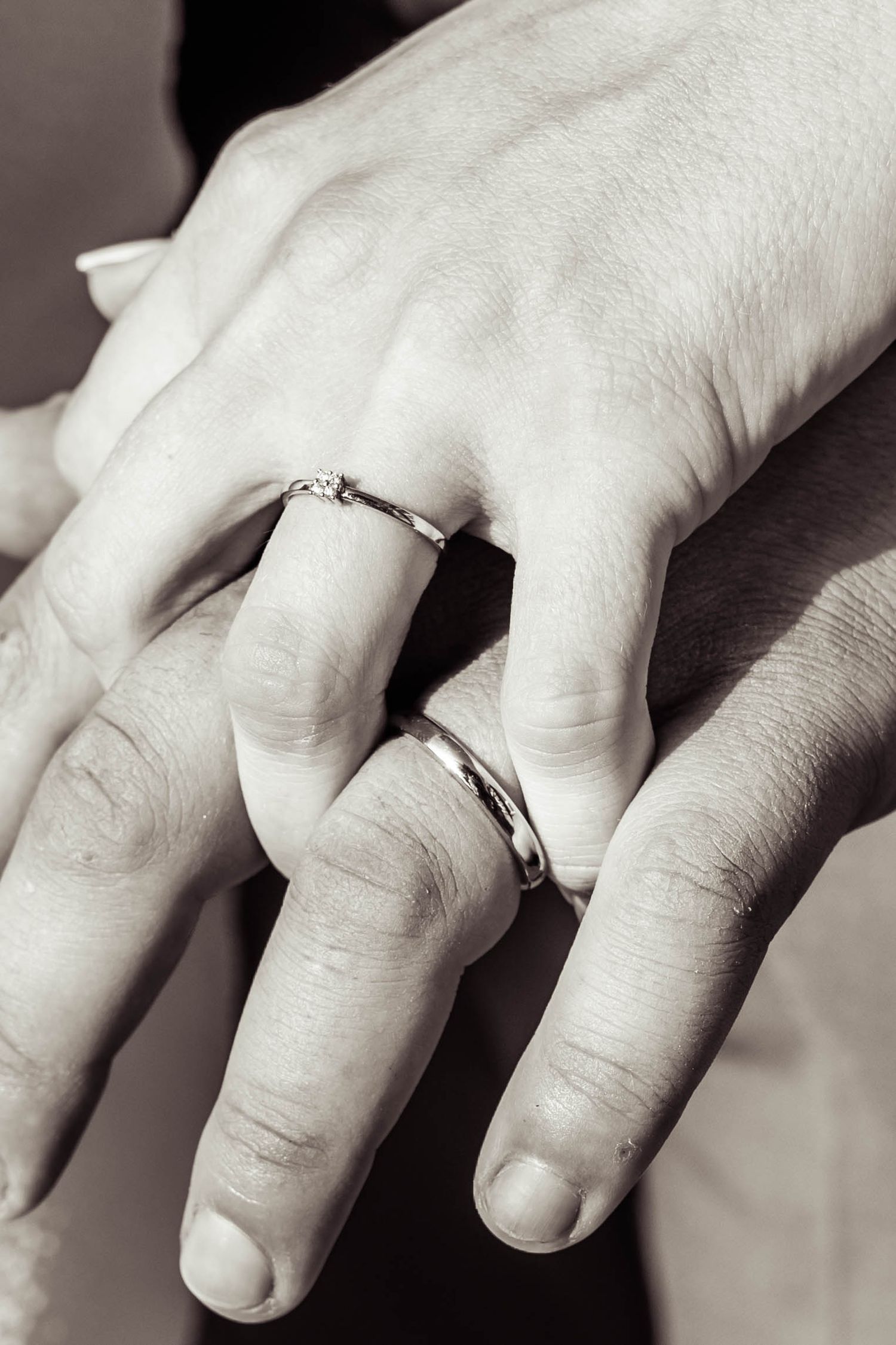 A black and white close-up of hands displaying wedding rings.