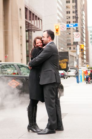 A couple embracing on a city street with tall buildings in the background.