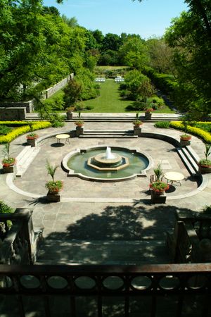 An elegant garden terrace with circular fountain and stone steps leading to a manicured lawn.