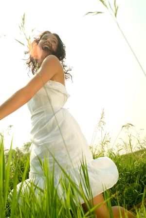 A person in white dress twirling joyfully in tall grass at sunset.