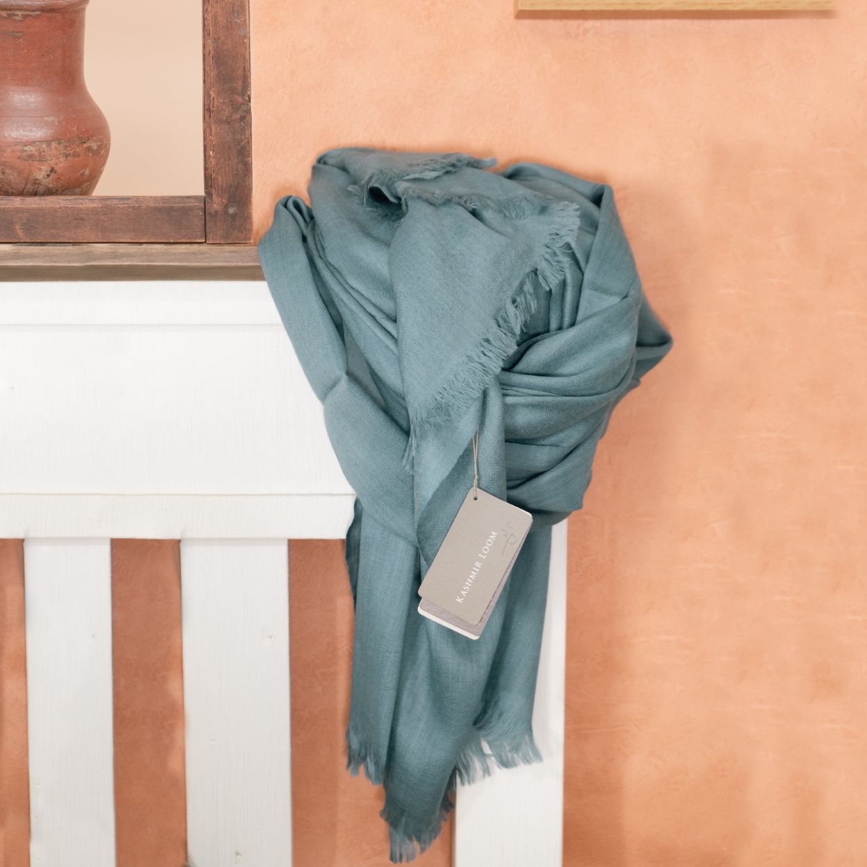 a lifestyle photo of a blue scarf on a terracotta backdrop with a wooden frame, white wood bed and art work