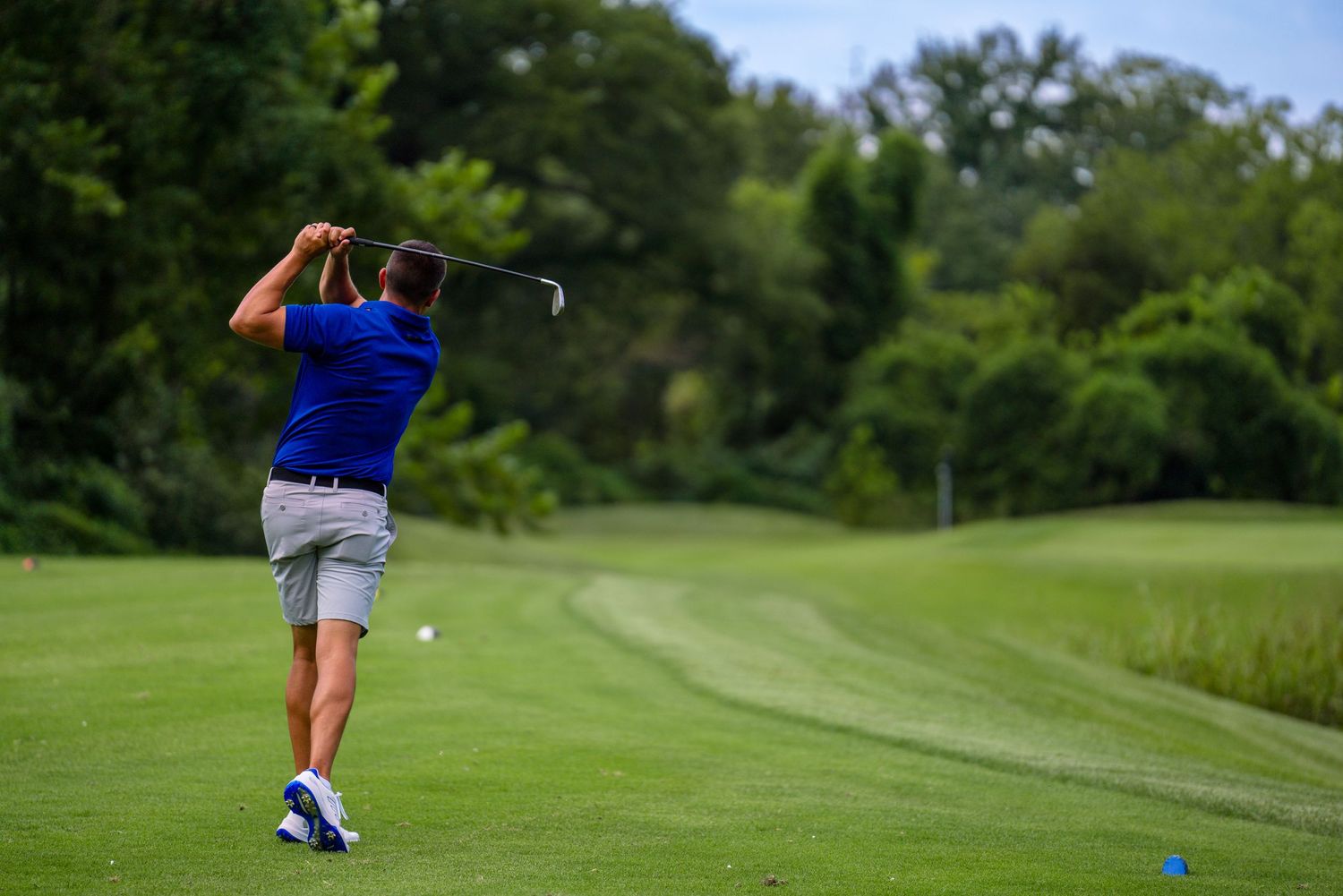 Golfer in blue shirt following through on swing on lush green fairway.