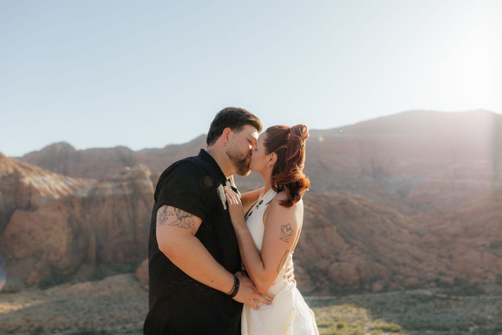 Couple sharing a romantic kiss at golden hour with red canyon mountains in the background.