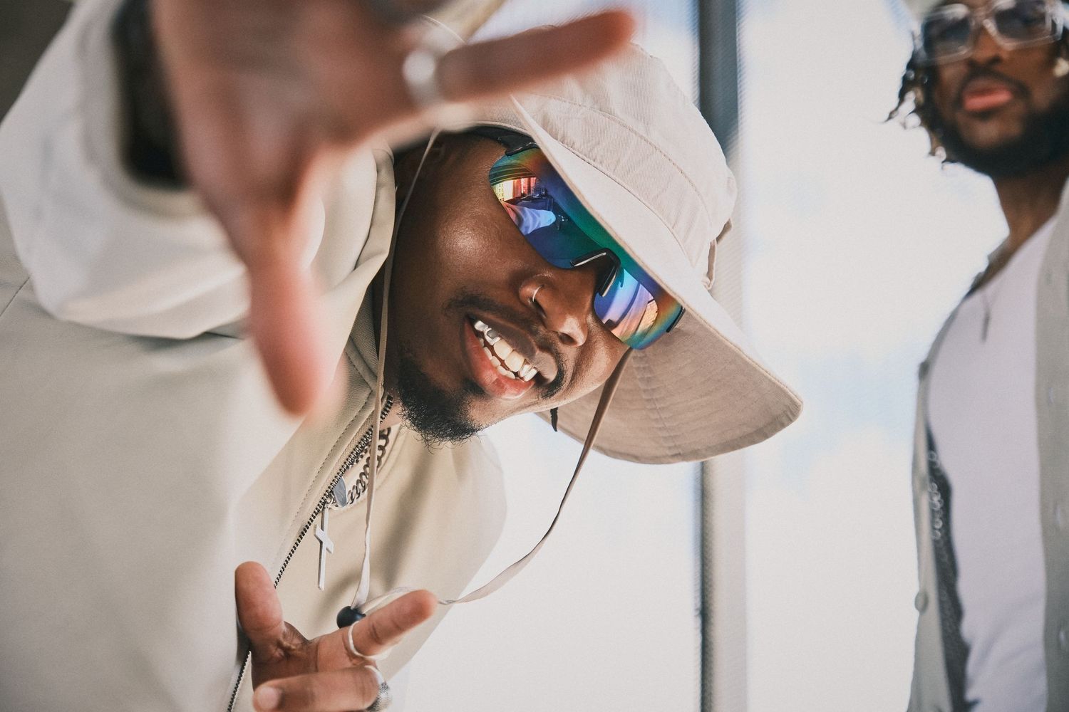 Stylish man with mirrored sunglasses and wide-brimmed hat, reaching towards the camera with a playful pose