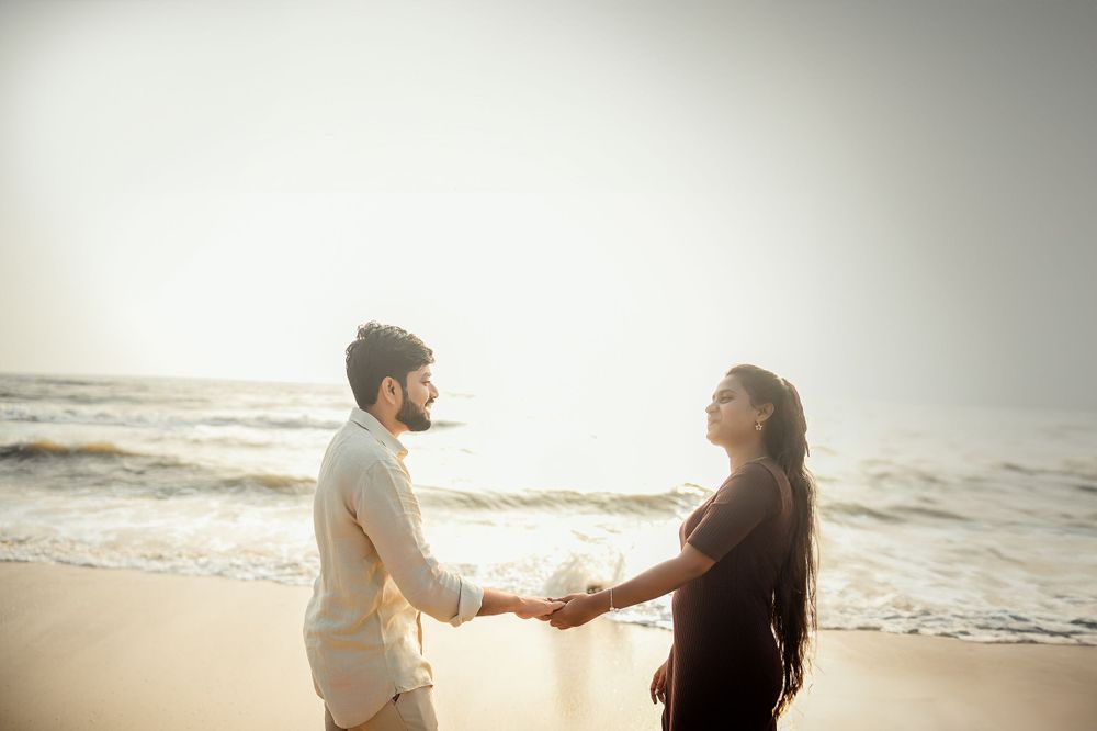 A couple holds hands on the beach during golden hour.