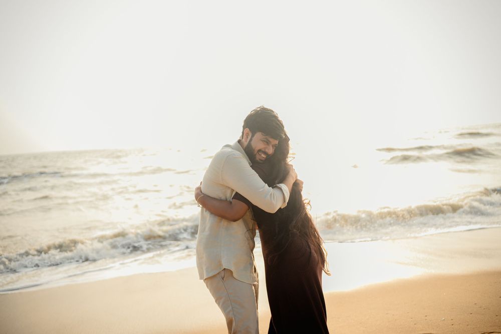 A couple embraces on a sunny beach with ocean waves in the background.