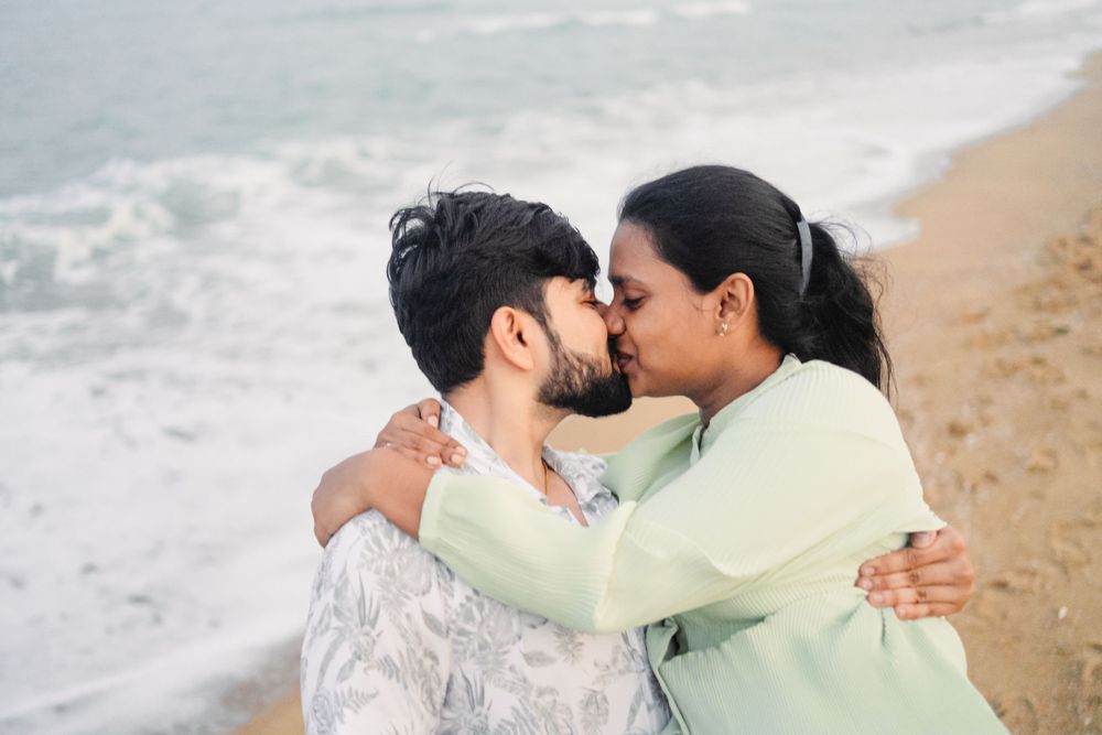 A tender embrace between a couple on a sandy beach with waves in the background.