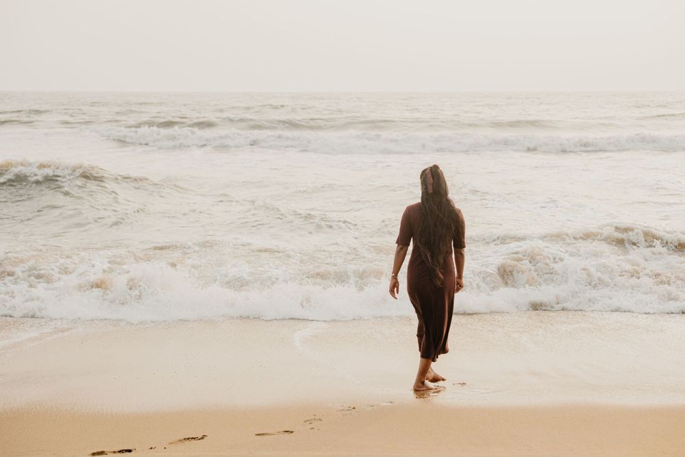 A person walks alone on a sandy beach at sunset with waves crashing in the background.
