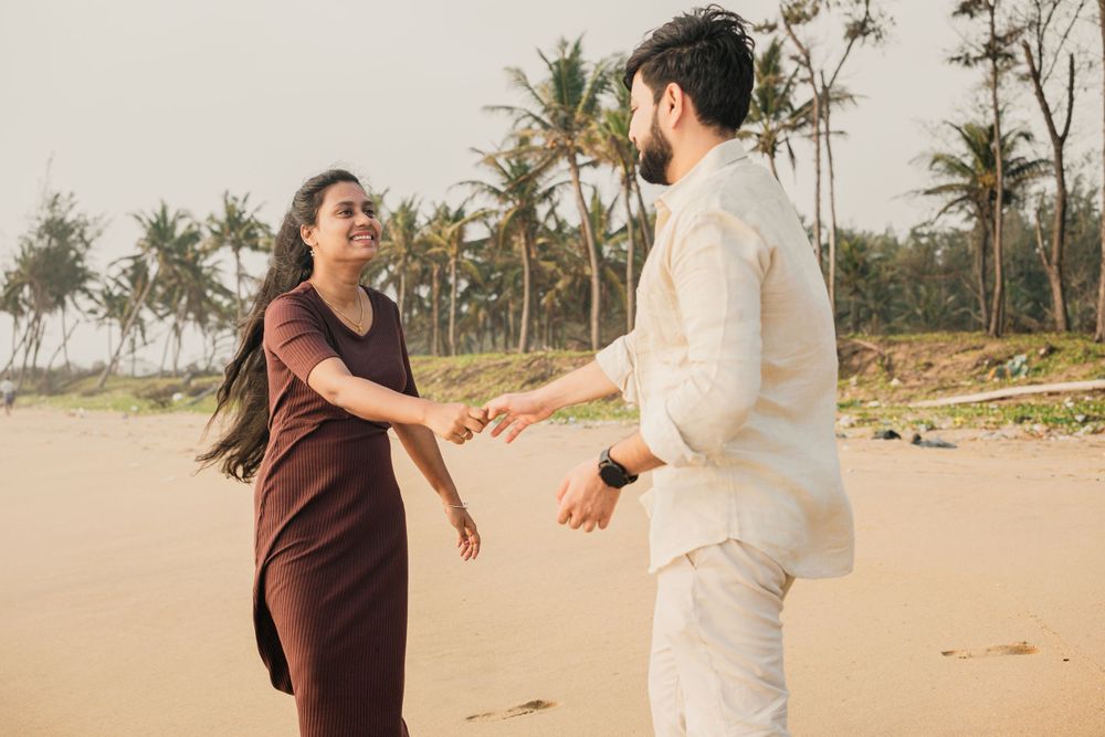 A couple dances playfully on a beach with palm trees in the background.