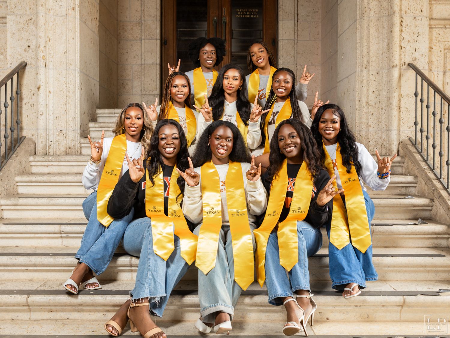 Group wearing yellow stoles and blue dresses pose on stone steps during graduation.