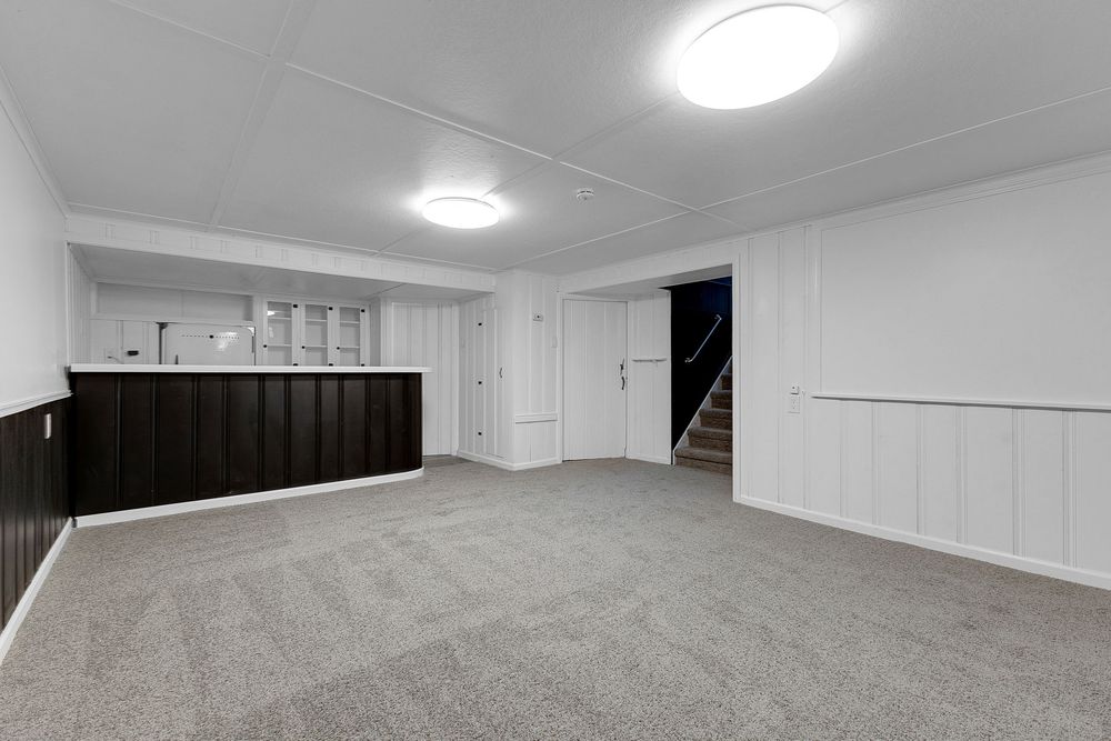 Finished basement with gray carpet, white wainscoting, dark bar area, and staircase leading upstairs.