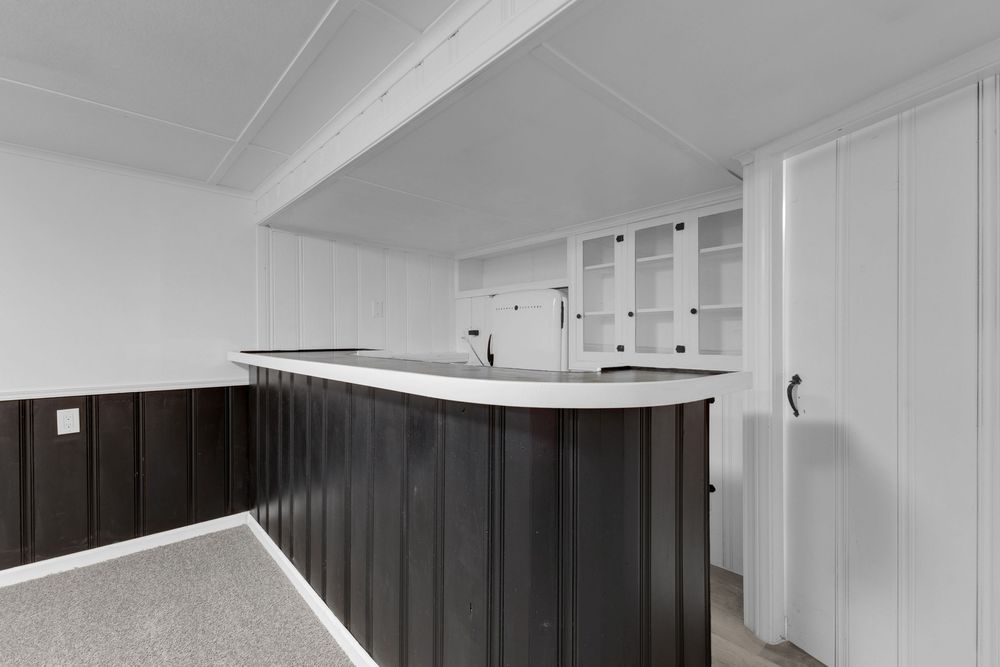 Black and white basement bar with curved dark wood paneling, built-in shelving, and white cabinetry in a finished space.