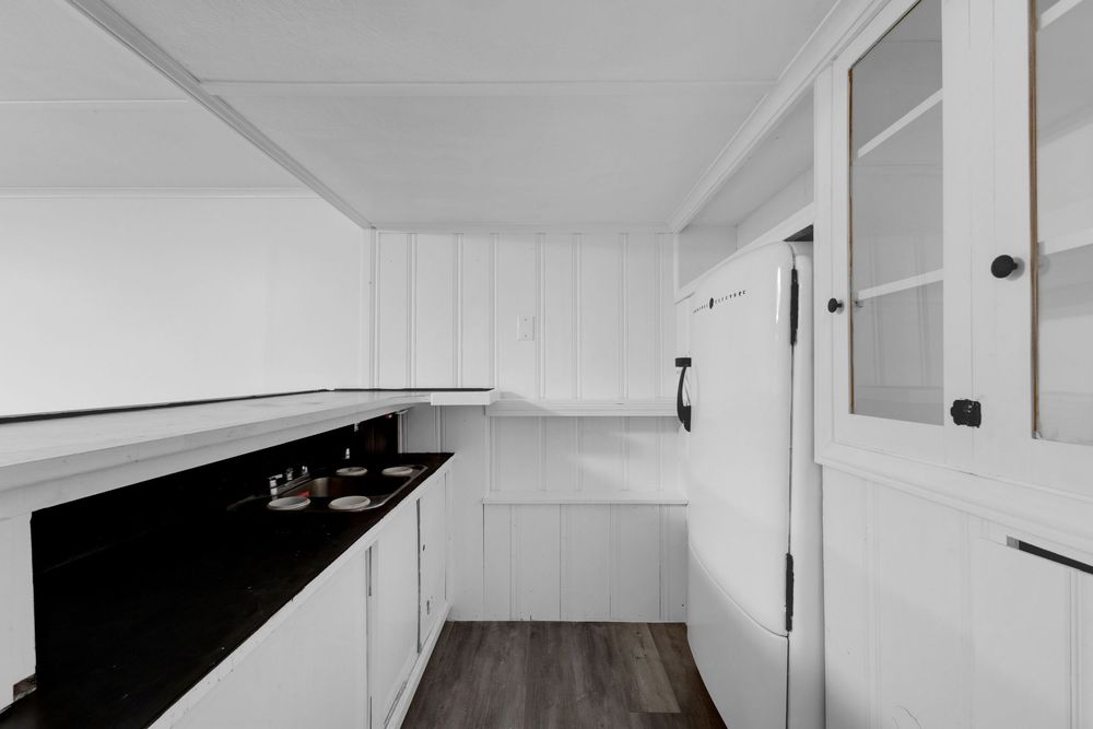 Modern white kitchen with black countertops, white cabinetry, dark hardwood floors, and glass-panel door accents.