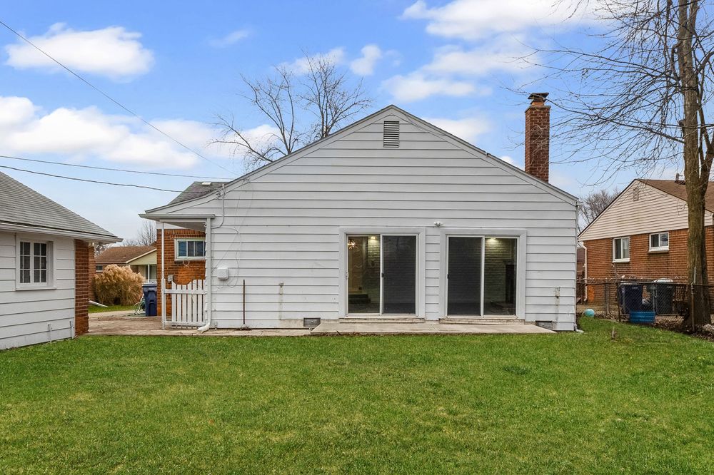 Rear exterior of a gray bungalow with sliding patio doors, chimney, and a well-maintained green lawn.