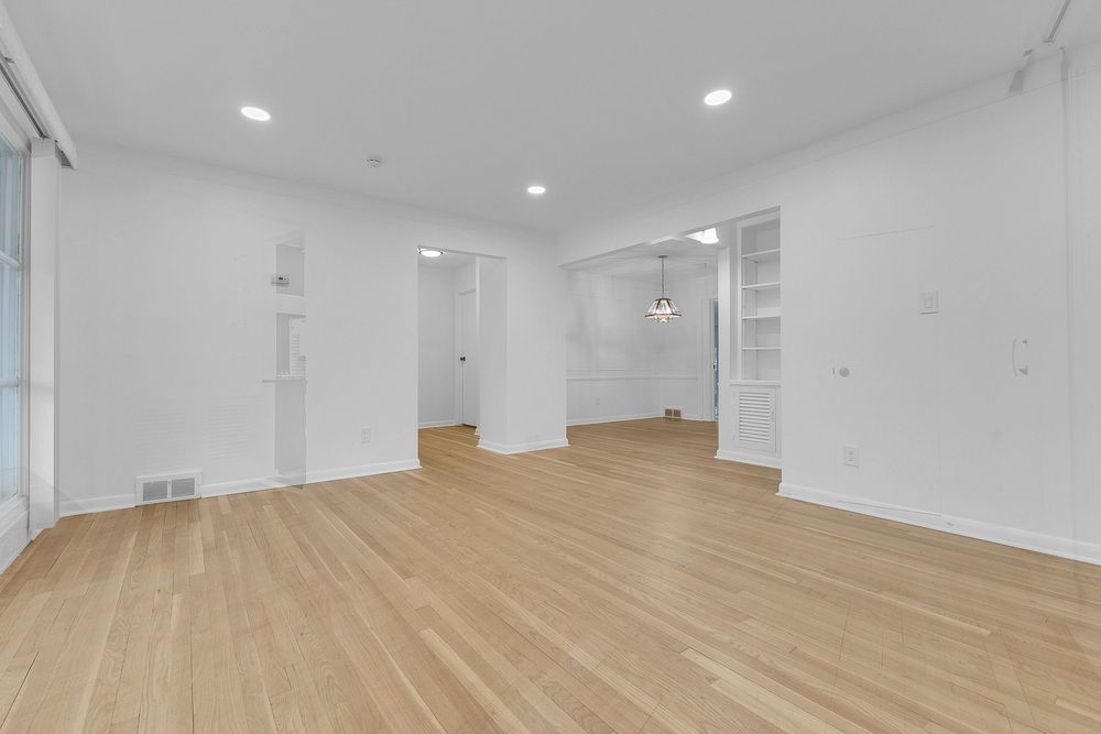 Bright empty living room with light hardwood floors, recessed lighting, white walls, and open floor plan.