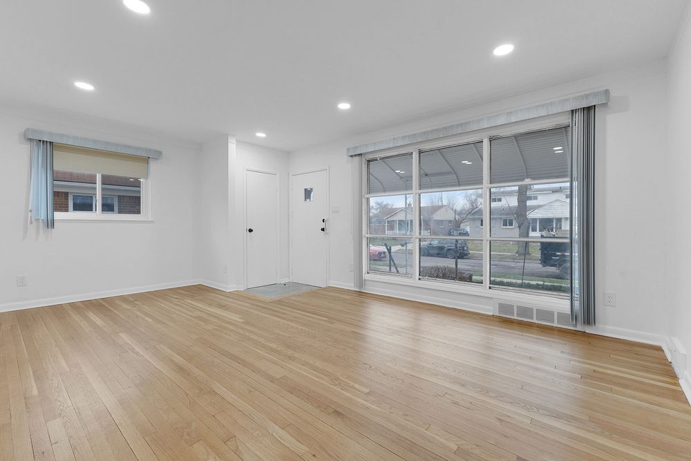 Bright empty living room with light hardwood floors, recessed lighting, and large sliding glass doors.