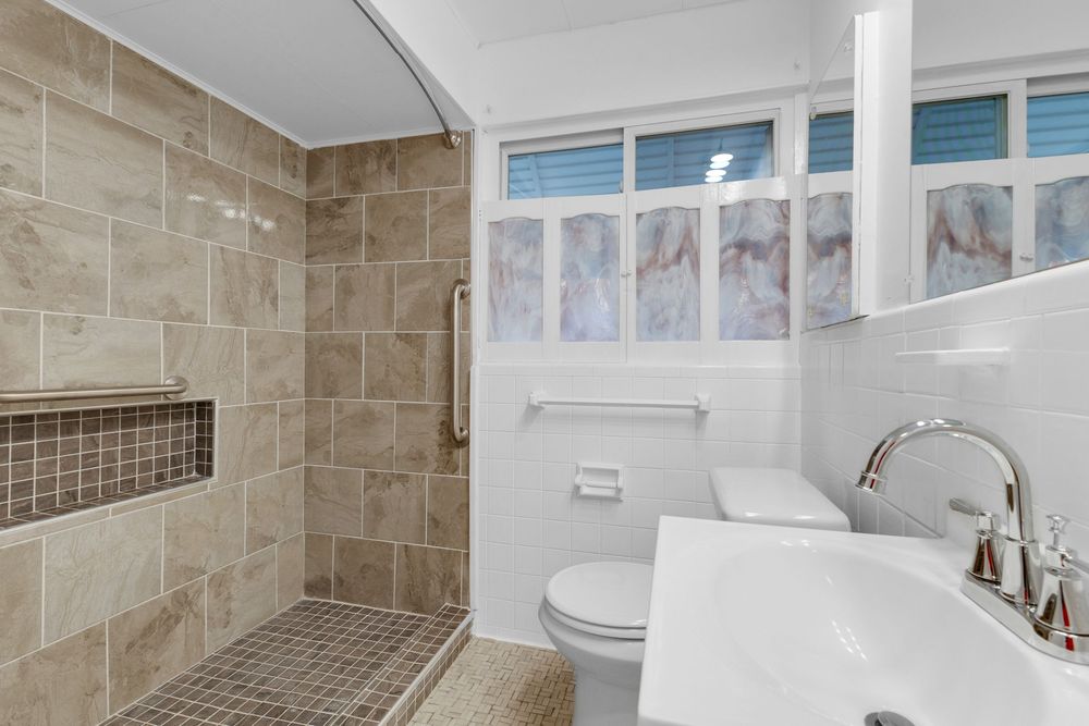 Modern bathroom with tiled walk-in shower, white toilet, pedestal sink, and frosted glass windows for natural light.