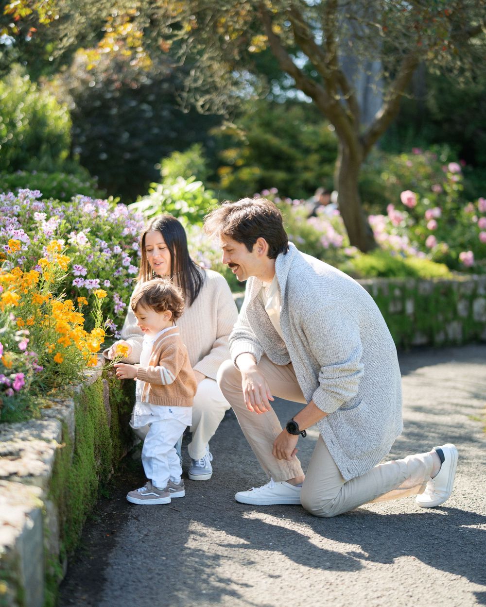 Family with toddler admiring colorful garden flowers together on a sunny day outdoors.