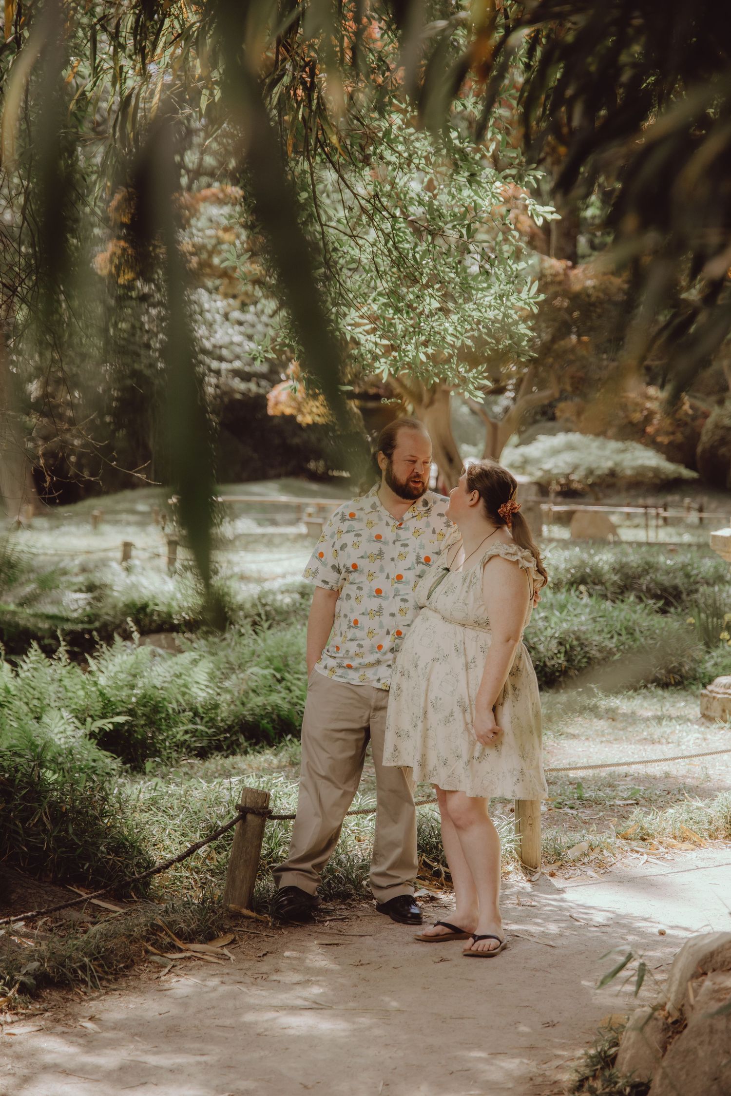 Couple sharing a romantic moment on a garden path surrounded by lush greenery and trees.