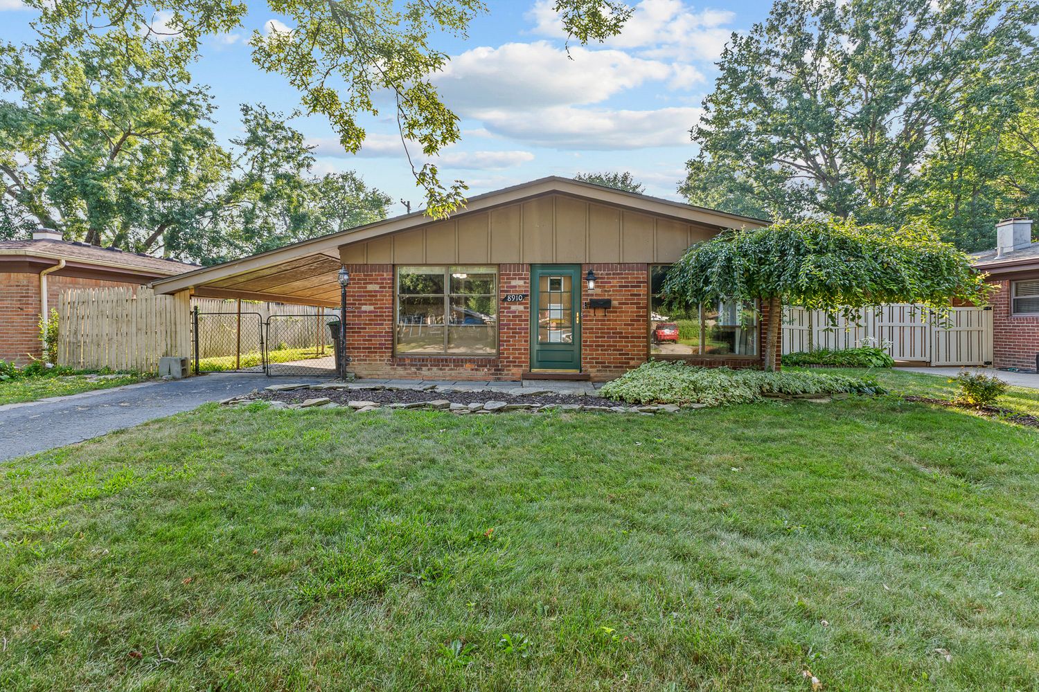 Brick ranch-style home with green front door, wood accents, fenced yard, and well-maintained landscaping.