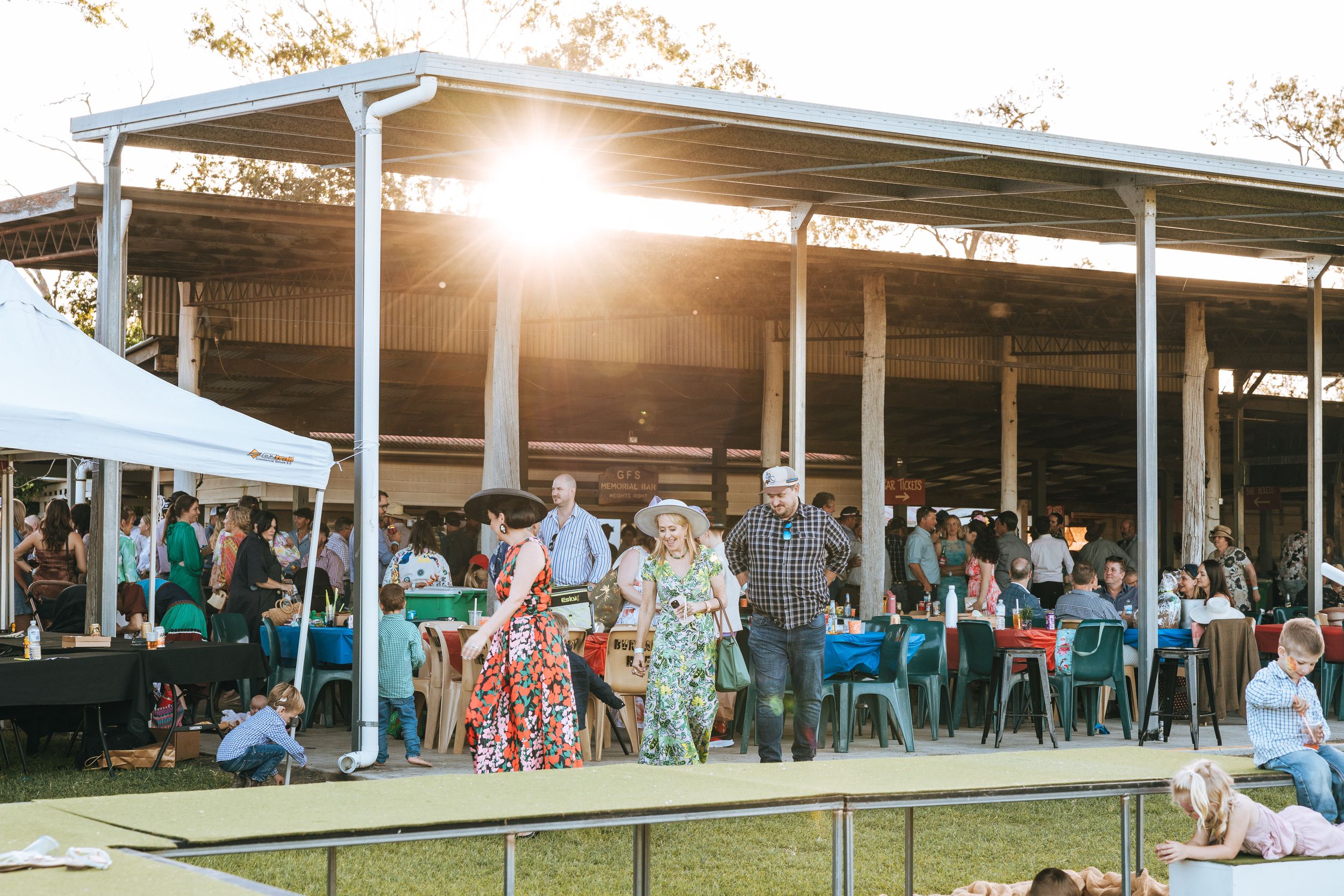 Outdoor festival gathering at sunset with guests mingling under a pavilion on a sunny evening.